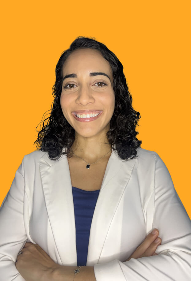Monica Pérez con fondo anaranjado y brazos cruzados mirando hacia la cámara sonriendo